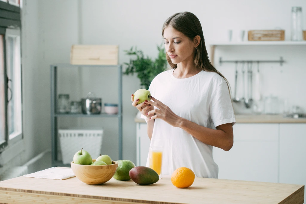 Aria Sterling, founder of Seventh Flavour, inspecting a fresh green apple in her kitchen before making a recipe.