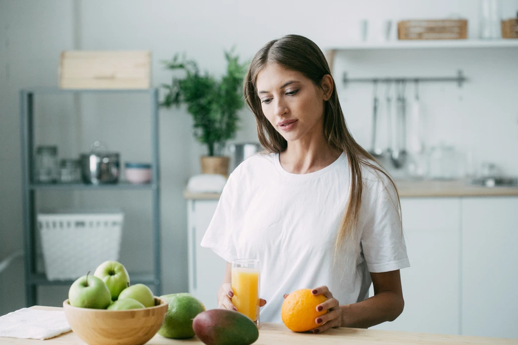 Food blogger Aria Sterling holding an orange while sitting in her bright, modern kitchen with a glass of juice.