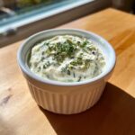 A close-up of creamy homemade tartar sauce topped with fresh dill in a small white bowl.