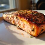 Close-up of a perfectly cooked, flaky air fryer salmon fillet seasoned with herbs, glistening under natural light.