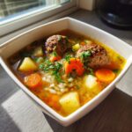 Close-up of a white bowl filled with flavorful albondigas soup, featuring meatballs, carrots, potatoes, and rice.