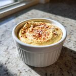 Close-up of creamy yellow homemade burger sauce topped with paprika and white crumbles in a white ramekin.