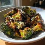 Close-up of perfectly roasted broccoli florets topped with grated Parmesan cheese in a white bowl.