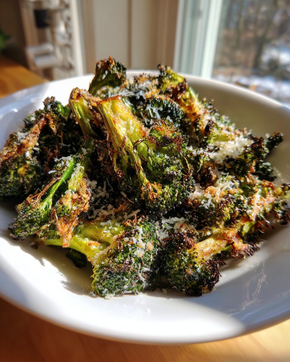 Close-up of perfectly crispy roasted broccoli florets topped with grated Parmesan cheese in a white bowl.