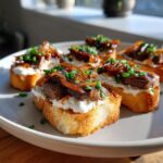 Close-up of several steak crostini appetizers topped with creamy cheese, seared steak, caramelized onions, and chives.