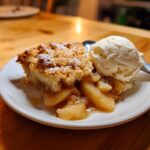A warm slice of apple cobbler recipe topped with powdered sugar, served with a scoop of vanilla ice cream.