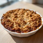 Close-up of a freshly baked apple crisp recipe with a thick, golden brown, crumbly oat topping.