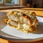 A close-up of two stacked slices of juicy baked ranch chicken breast covered in melted white sauce and dried herbs.