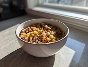 A close-up of a white bowl filled with seasoned black eyed peas mixed with cooked onions and celery, sitting in bright sunlight.