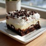 A rich slice of brownie refrigerator cake featuring a dark brownie base, a creamy layer, and a thick whipped topping sprinkled with mini chocolate chips.