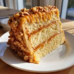 A thick slice of caramel crunch cake showing three layers of sponge cake filled with caramel and covered in caramel frosting and nuts.