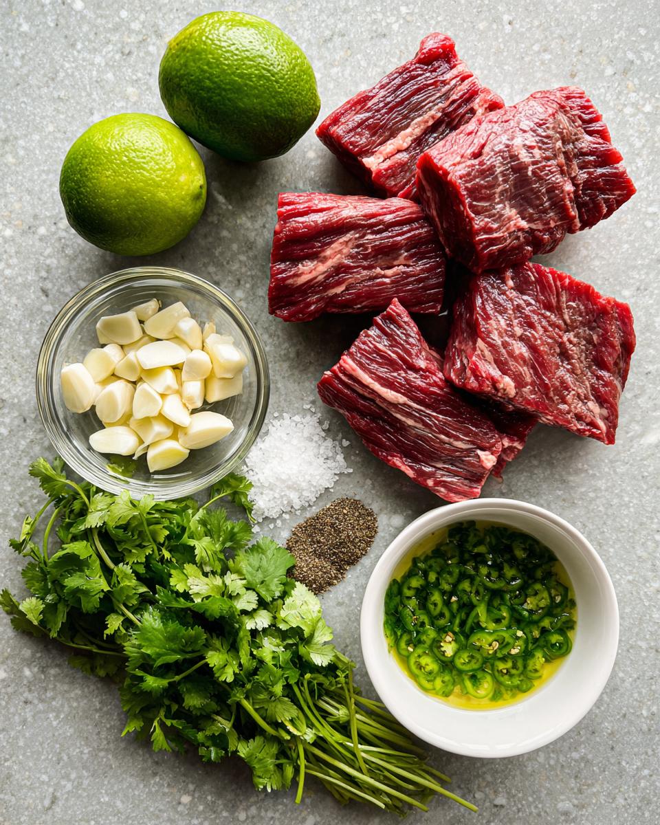 Raw beef cuts alongside ingredients for Carne asada marinade: limes, garlic, cilantro, salt, pepper, and sliced jalapeños in oil.