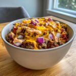 A close-up of a hearty cheeseburger bowl topped with melted cheddar, diced red onion, and a drizzle of sauce.