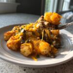 A fork lifting a bite of cheesy tater tot casserole, showing melted cheese stretching between the fork and the plate.