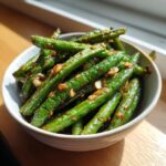 Close-up of vibrant green beans coated in a savory garlic sauce, ready to serve.