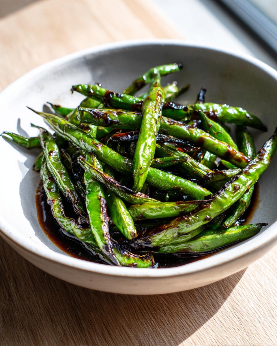 Close-up of blistered chinese green beans with garlic sauce served in a light ceramic bowl.