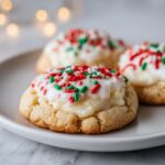Three christmas gooey butter cookies topped with thick white frosting and red and green sprinkles on a white plate.