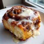 A close-up, appetizing shot of a single cinnamon roll with heavy cream glaze dripping down the sides.