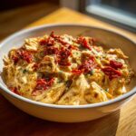 A close-up of rich, creamy crockpot marry me chicken topped with vibrant sun-dried tomatoes in a light bowl.