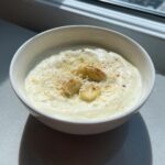A close-up of creamy homemade alfredo sauce topped with grated cheese and roasted garlic cloves.