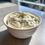A creamy, chunky pickle dip topped with fresh dill, served in a white bowl.