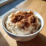 Close-up of a bowl of creamy rice pudding generously dusted with ground cinnamon.