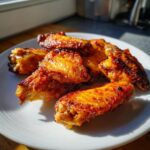 A pile of golden brown, crispy baked chicken wings glistening under sunlight on a white plate.