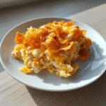 A close-up serving of creamy Dorito Casserole topped with crunchy, cheesy chips on a white plate.