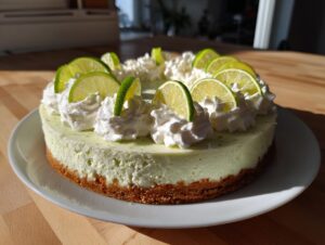 A whole, un-sliced key lime cheesecake topped with dollops of whipped cream and fresh lime slices.