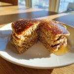 A stack of fluffy banana oatmeal pancakes cut in half, drizzled with syrup, sitting on a white plate.
