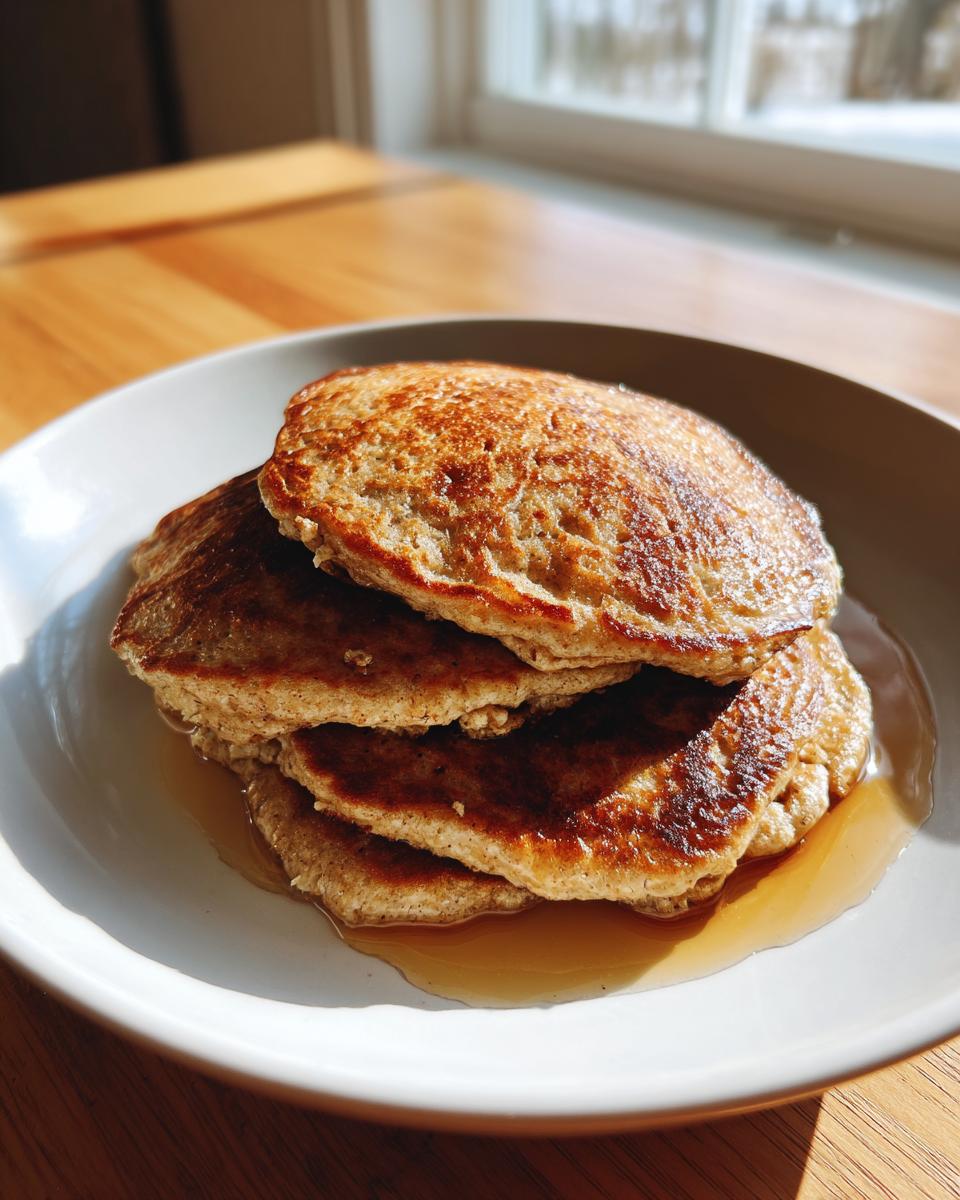 A stack of three fluffy banana oatmeal pancakes drizzled with maple syrup on a white plate.
