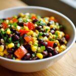 Close-up of fresh cowboy caviar featuring black beans, yellow corn, diced red peppers, and cilantro in a white bowl.