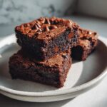 Three rich, fudgy sweet potato brownies stacked on a light ceramic plate, topped with chocolate chips.