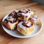 A plate of freshly baked, gooey cinnamon roll bites generously topped with white vanilla icing.