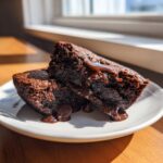 Two rich, dark slices of hot fudge pie showing a gooey, melted chocolate center dripping onto a white plate.