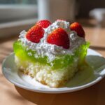 A moist slice of green jello poke cake topped with whipped cream and fresh strawberries.