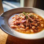 A close-up, appetizing bowl of rich Ham and Bean Soup topped with shredded ham and fresh thyme.