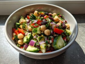 Close-up of a vibrant, colorful bean salad featuring chickpeas, kidney beans, cucumber, red onion, and peppers in a white bowl.