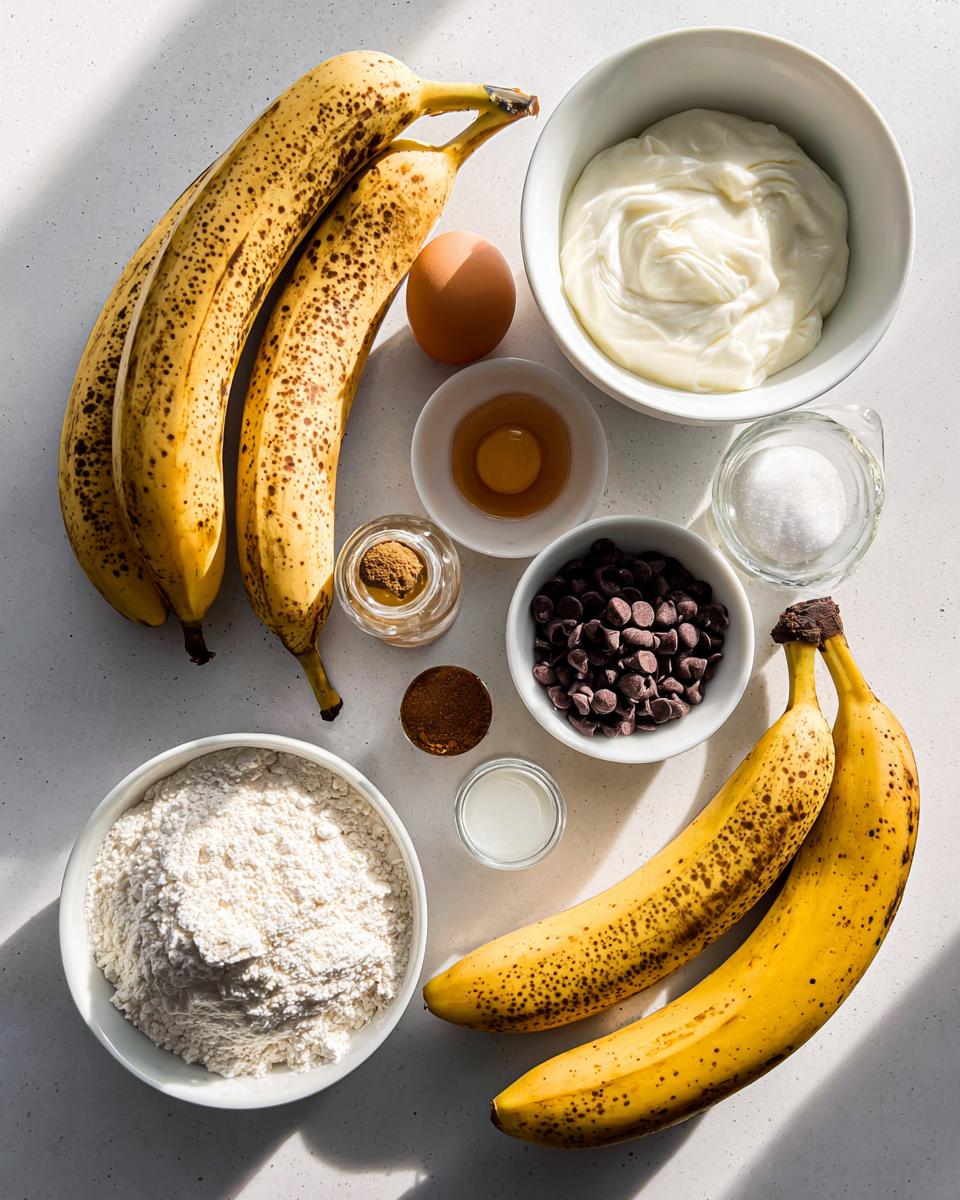 Overhead view of ingredients for greek yogurt banana bread, including ripe bananas, flour, greek yogurt, egg, and chocolate chips.