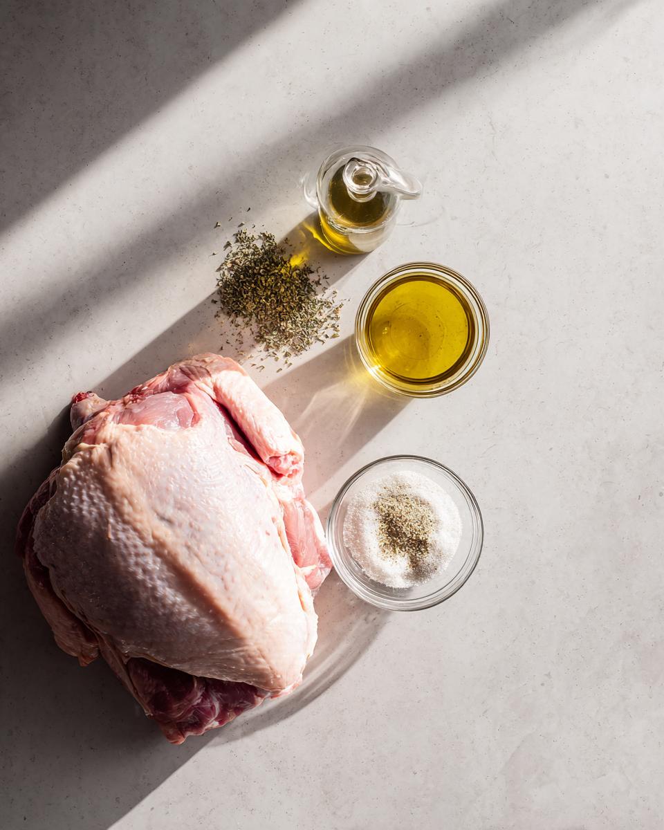 Overhead view of raw turkey breast next to bowls of olive oil, salt, pepper, and dried herbs for slow cooker turkey breast.