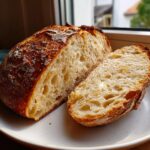 A loaf of freshly baked Italian bread, cut in half to show the airy, open crumb structure.