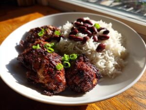 Close-up of three pieces of dark, glazed Jamaican Jerk Chicken served with rice and kidney beans.