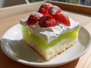 A moist slice of jello poke cake featuring a layer of bright green gelatin, topped with whipped cream and fresh strawberries.