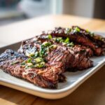 Close-up of sliced, grilled steak topped with a bright green herb sauce, likely showing the results of a carne asada marinade.