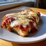 Close-up of a serving of keto chicken parmesan, topped with melted mozzarella and marinara sauce, seasoned with herbs.