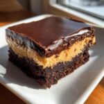 A single, thick square of layered buckeye brownies featuring a dark chocolate base, creamy peanut butter middle, and glossy chocolate topping.
