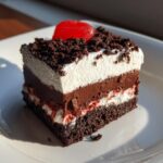 A perfect square slice of layered oreo dirt cake featuring chocolate cake, pudding, cream, and cookie crumbs.