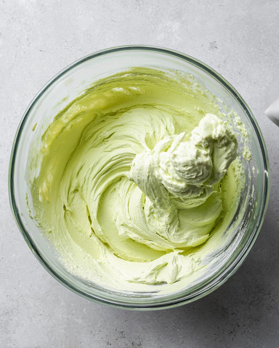 Overhead view of pale green, creamy key lime cheesecake filling being mixed in a clear glass bowl.