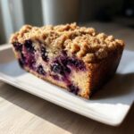 A close-up slice of moist blueberry banana bread topped with a thick, golden streusel topping.