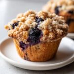 Close-up of a moist blueberry muffin topped with brown sugar streusel, showing burst blueberries.